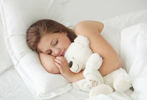 Kız bir oyuncak ayı ile bir kucaklama içinde uyuyor.