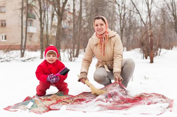 Kvinne med et barn renser et teppe i snøen