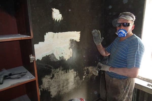 Човек чисти чађу са зида после пожара