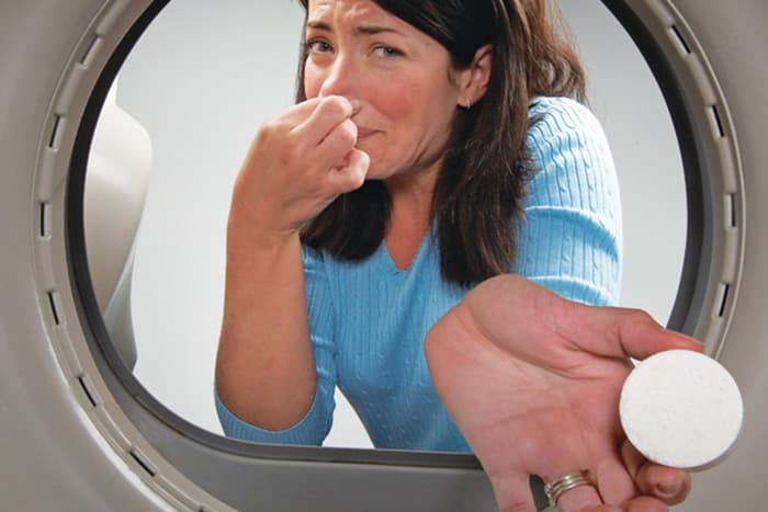 Sieviete pievieno tableti veļas mazgājamās mašīnas mucai