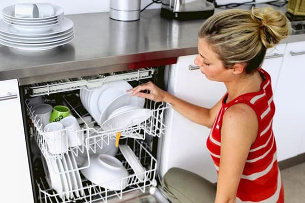 Kız tabakları bulaşık makinesinden alır.
