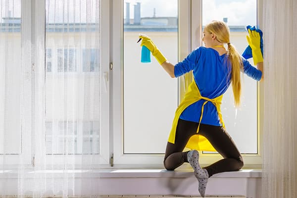 Das Mädchen auf der Fensterbank wäscht ein Fenster