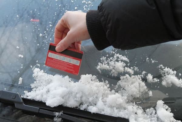 Limpando o carro da neve com um cartão de plástico