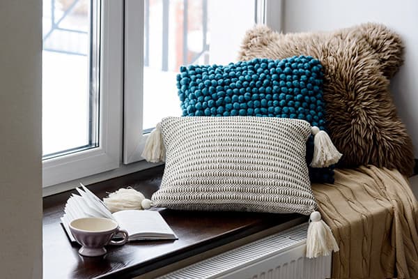 Almohadas, taza y libro en el alféizar de la ventana
