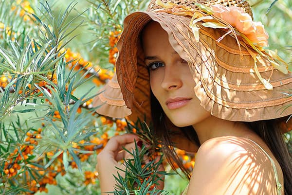 Chica con un sombrero cerca de un arbusto de espino amarillo
